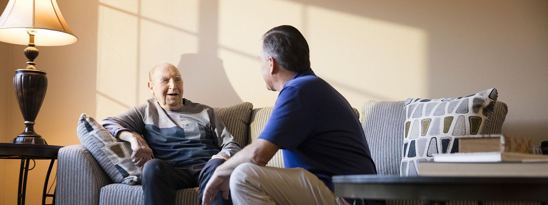 Caregiver and resident sitting a the couch smiling and talking