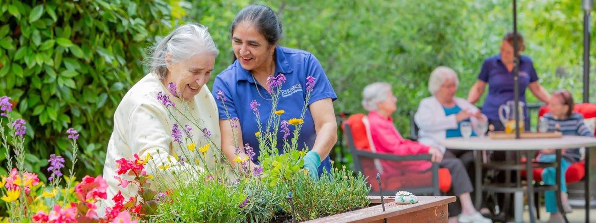 Resident and staff gardening and other residents socializing around a patio table.