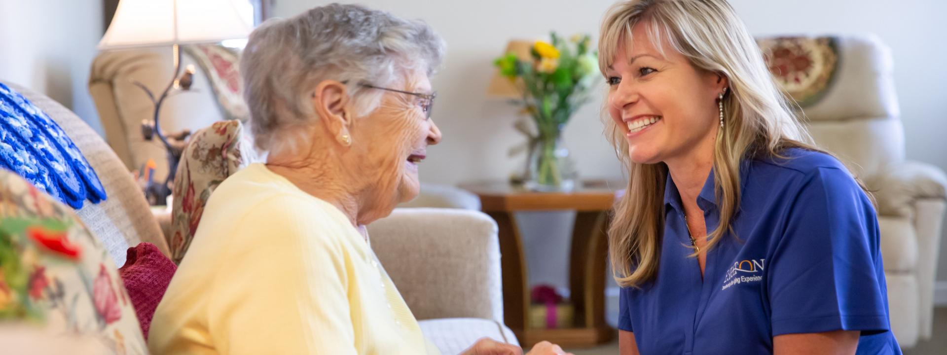 A women caregivers smiling and holding hands of a woman resident. 