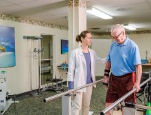Male resident receiving walking therapy with staff assisting him.