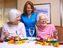 Two women residents smiling and enjoying lunch in the dining room.