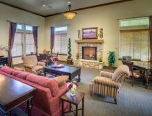 Community living room with a fireplace, couch, two comfy chairs, and a table with four chairs