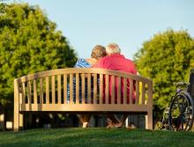 A loving couple sitting a park bench with their arms around each other.