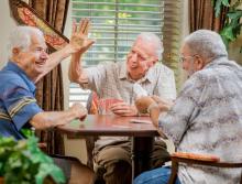 Three men playing a game of cards; two giving each other a high five..