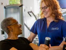 A smiling staff member with a smiling resident on a stationary bike.