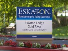 Eskaton Lodge Gold River sign with red and white flower planted below it.