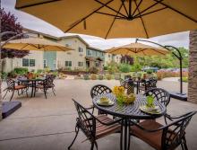 Outdoor patio with round table, chair, umbrellas, flower garden and potted plants.