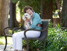 women sitting on an outside bench smiling and hugging her dog
