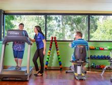 A woman on a treadmill and a man on a stationary bike in the exercise room with a staff member