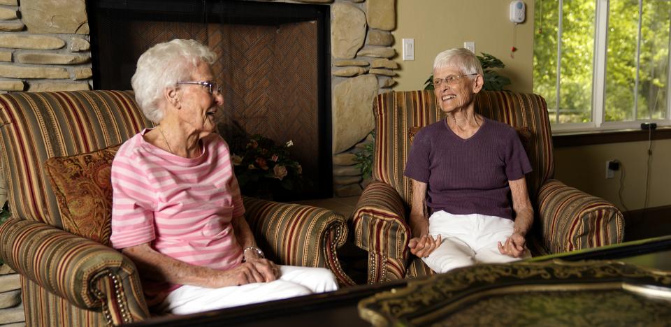 Two residents sitting by the fireplace smiling and talking