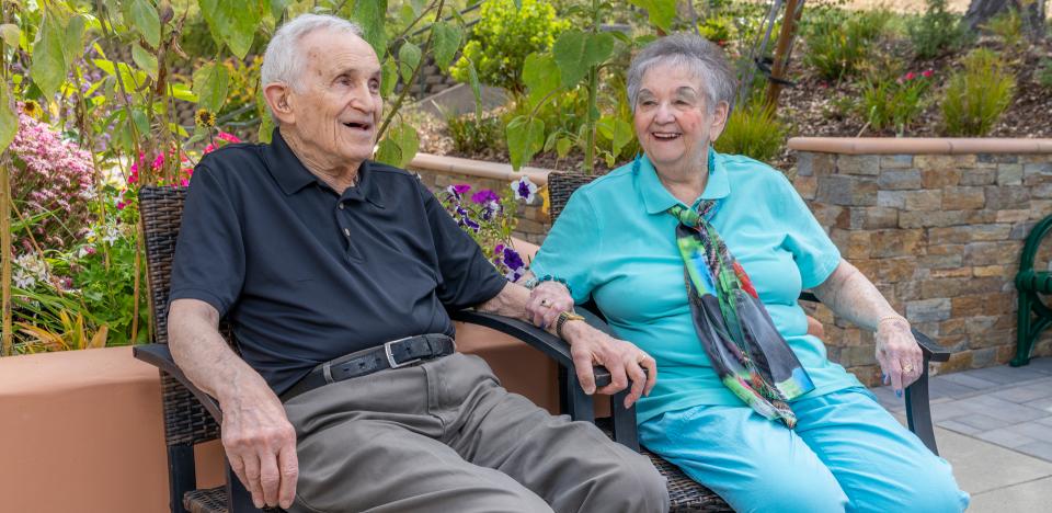 A couple sitting on the patio, holding hands and smiling.