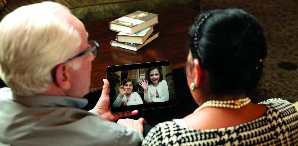Grandparents sitting on their couch face-timing with the grandchildren on their iPad