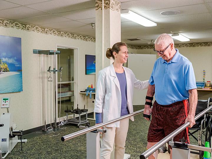 Male resident receiving walking therapy with staff assisting him.