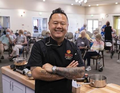 Chef Tila smiling with his arms folded at a cooking demonstration at Eskaton Village Carmichael
