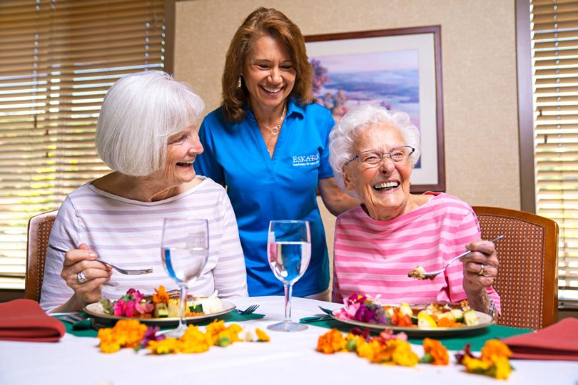 Two women residents smiling and enjoying lunch in the dining room.