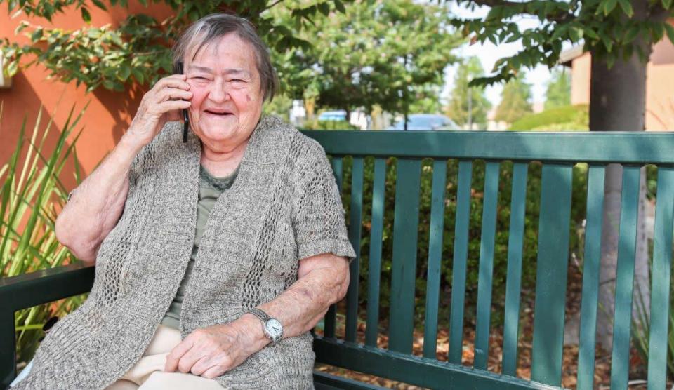 Smiling woman sitting outside on a green bench talking on a mobile phone.