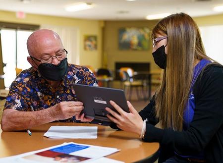 Resident receiving training on his new digital devise from a staff member