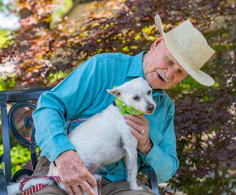 Man sitting a patio chair, holding his white dog