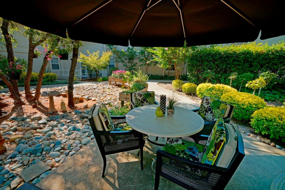 Patio table and chair under a large umbrella.