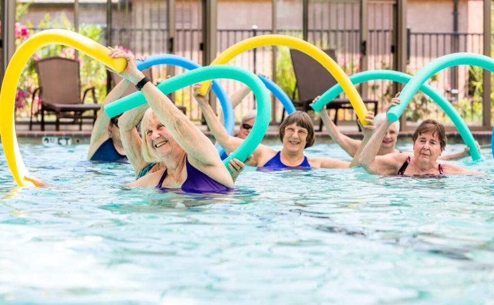 Six women in a pool doing aerobics holding foam pool noodles