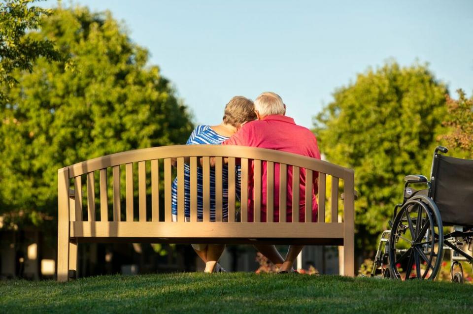 A loving couple sitting a park bench with their arms around each other.
