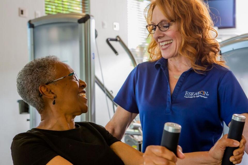 A smiling staff member with a smiling resident on a stationary bike.