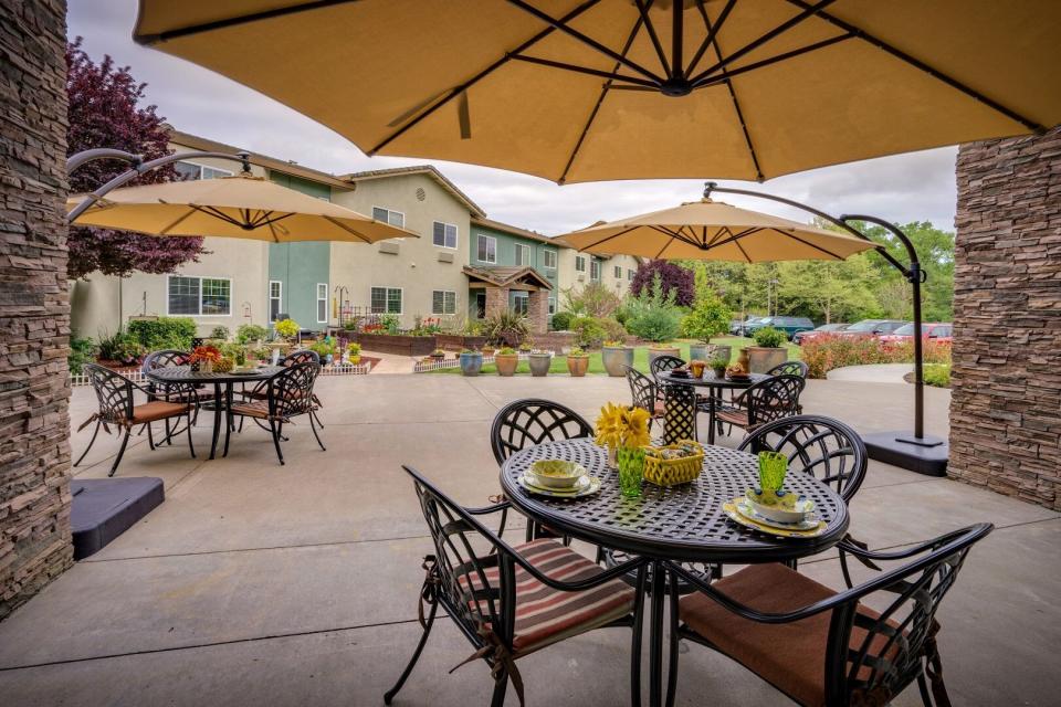 Outdoor patio with round table, chair, umbrellas, flower garden and potted plants.