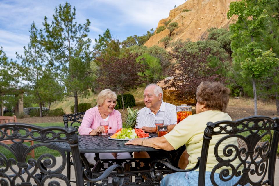 Two women and one man sitting at a patio table socializing with drinks and  a fruit