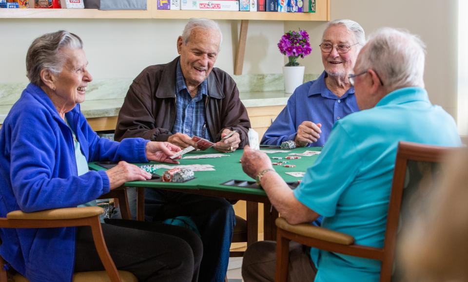 Four residents smiling and laughing and playing a game of cards