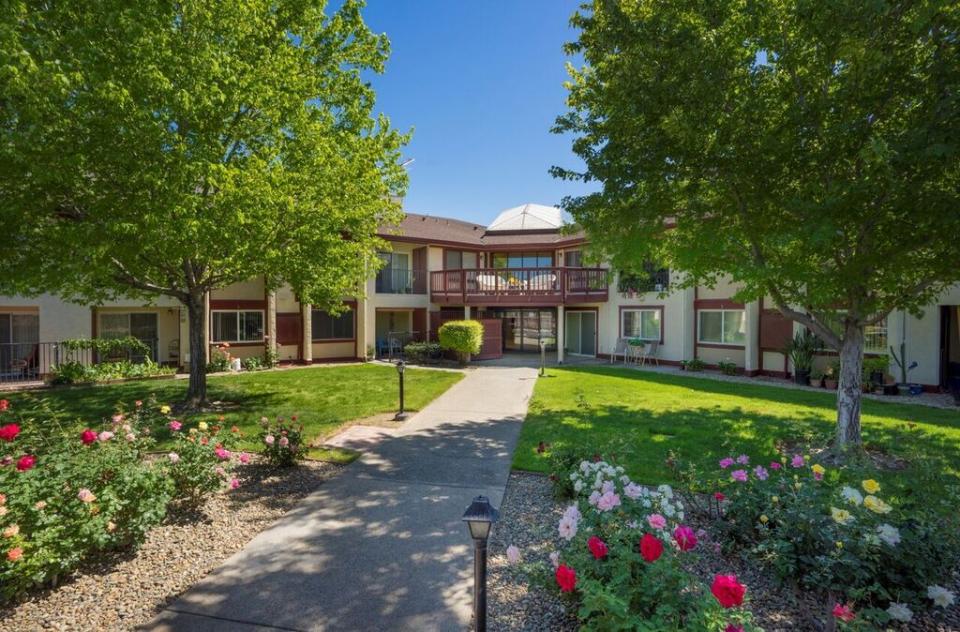 Front entrance of Eskaton Jefferson Manor with green trees and bushes, flowers and green lawn.