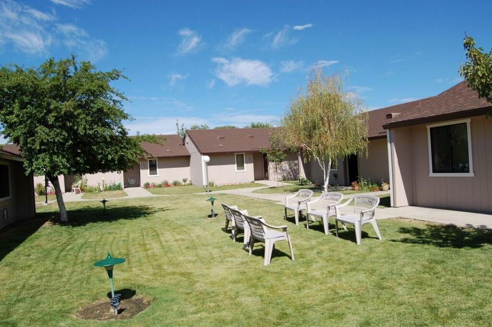 Exterior of Eskaton Lassen Manor's apartments with beautiful trees and chairs on their green lawn..