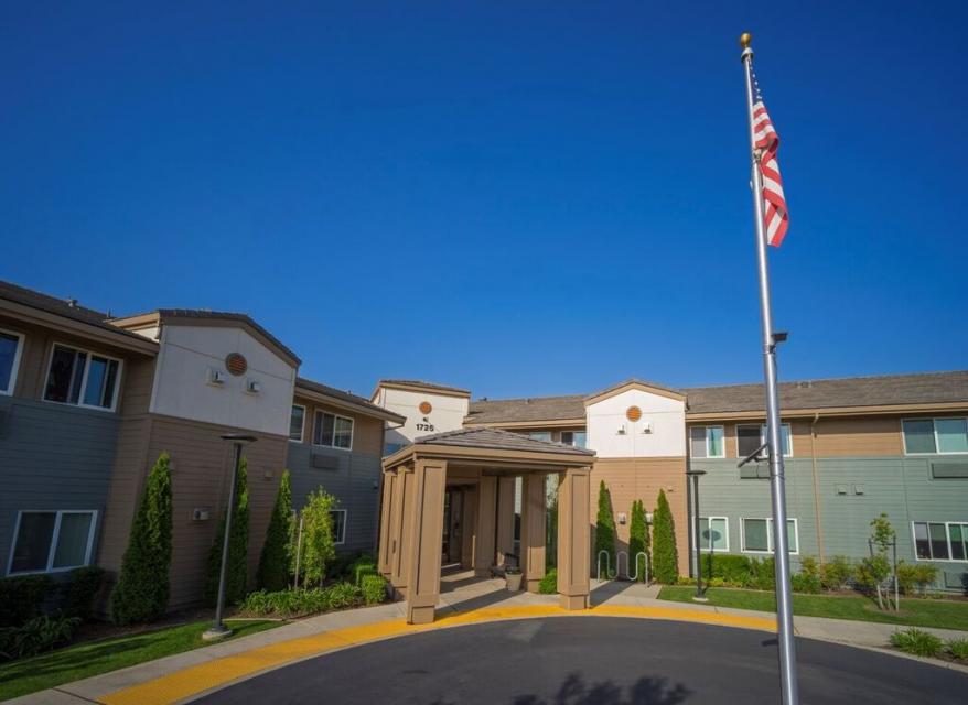 Eskaton Roseville Manor's front entrance with green trees, bushes and lawn, and the American Flag.