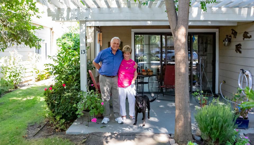 Happy couple with the dog, standing in front of their cottage home.
