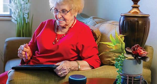 Woman resident sitting on her couch with her iPad and Alexa.