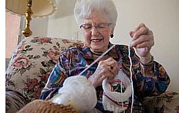 Resident Marian sits in her armchair, tugging on a spool of yarn, making caps for babies.