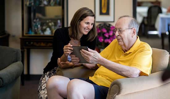 Woman staff member teaching a male resident how to use an iPad with smart home system.