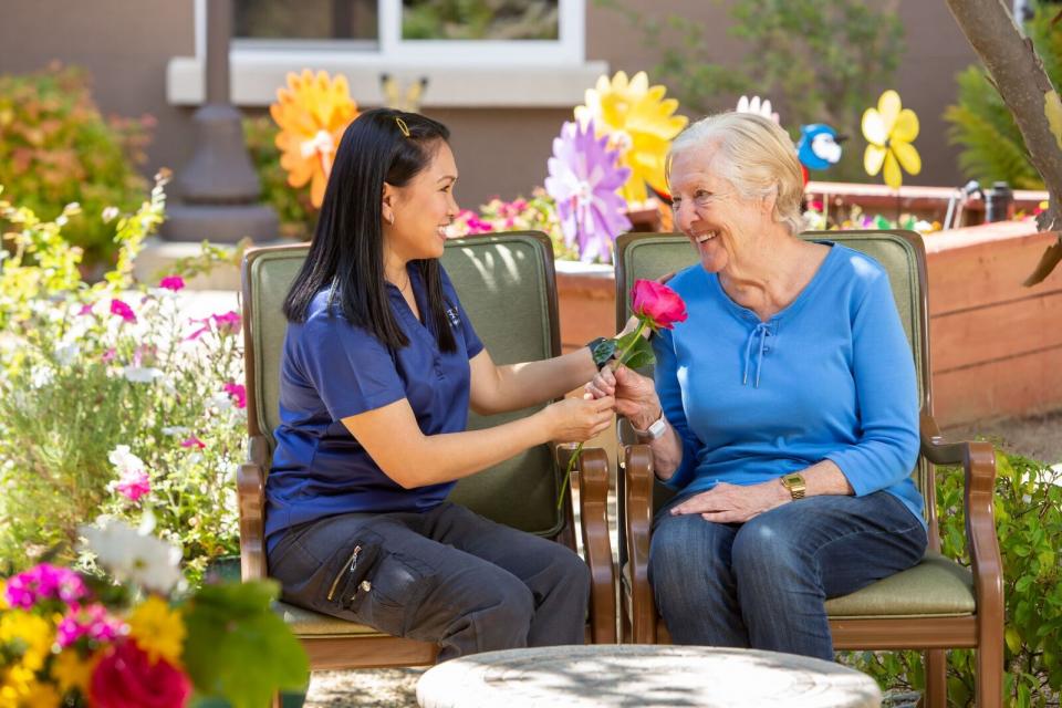 two women sitting by the garden. One woman giving the other a beautiful red rose.