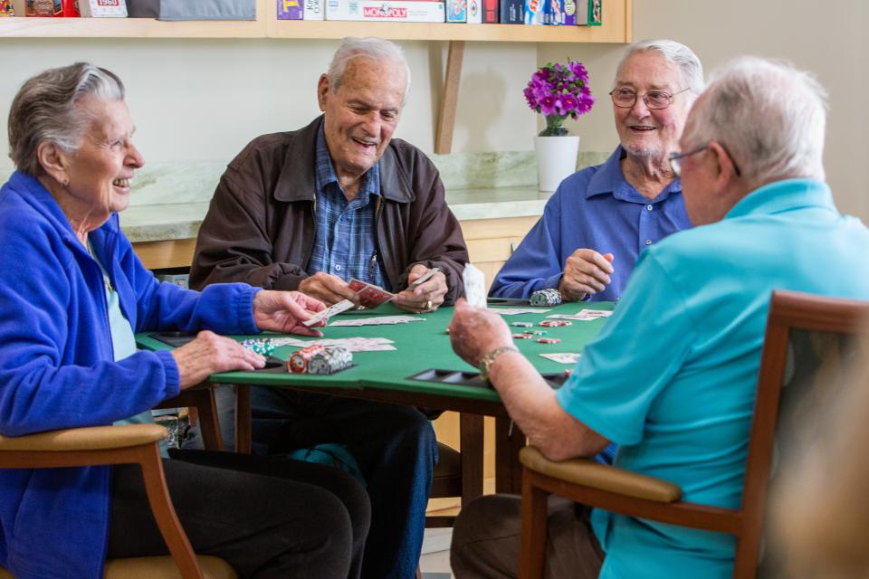 Four residents smiling and laughing and playing a game of cards