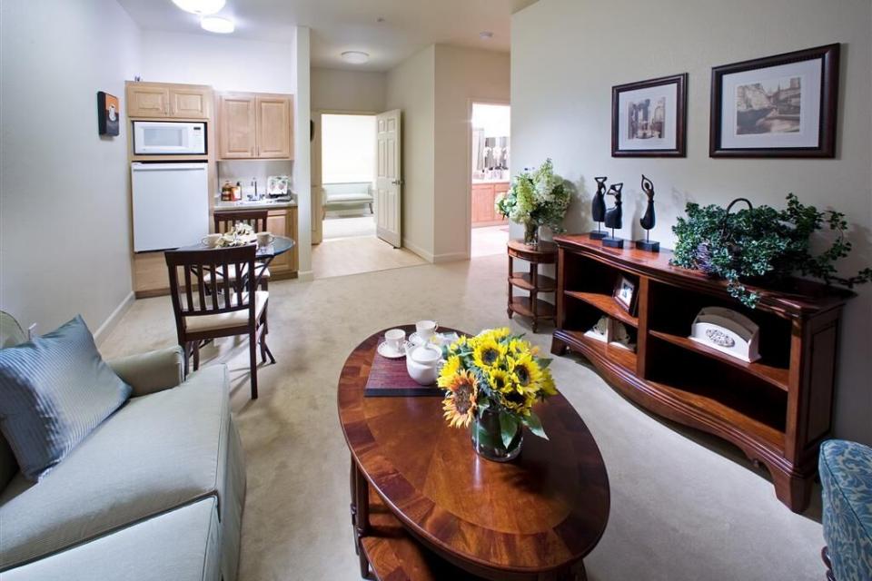 Assisted living apartment living room with couch and chairs, coffee table and bookshelf. 