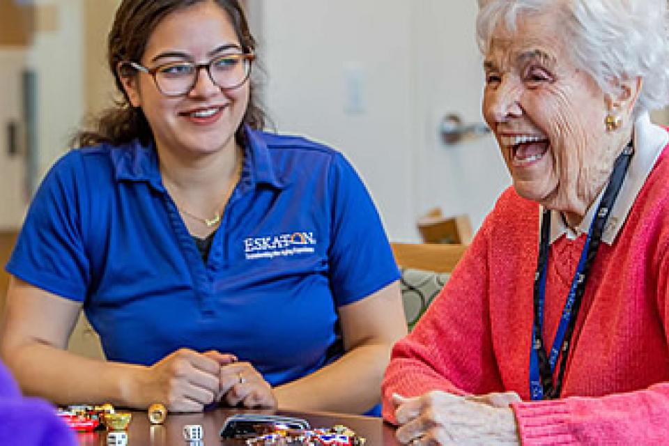 Resident and staff laughing and playing a dice game.