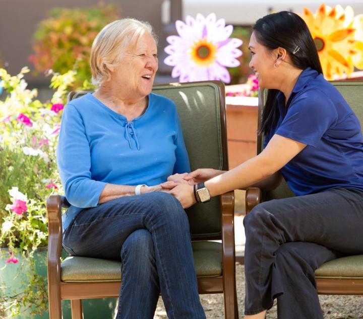 Woman resident and a staff member sitting in the garden talking an holding hands.