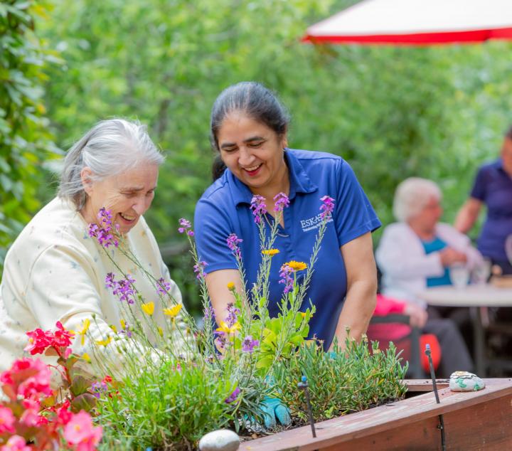 Two women planting plants in a planter on the patio area.  
