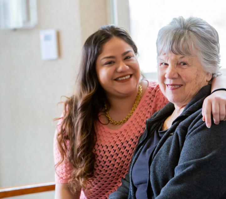 Smiling staff member with her arm are a smiling woman resident.