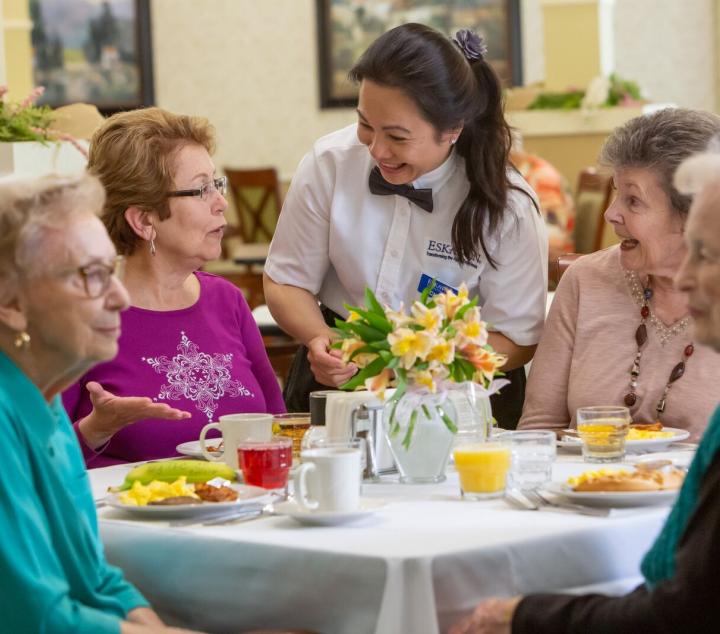 Four women residents being served food by a waitress in the dining room. 