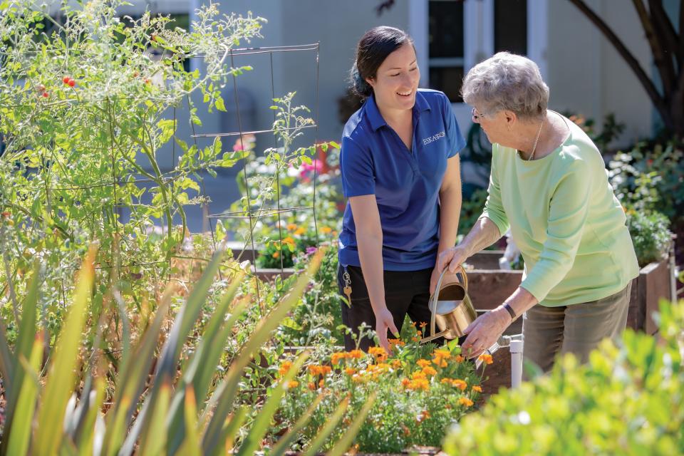 Two women, resident and staff, watering plants in the flowerbed 