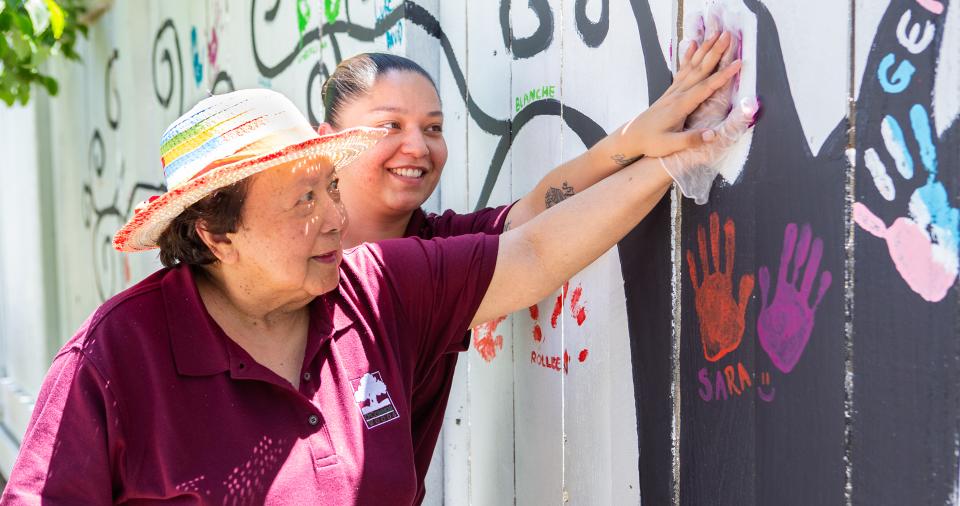 Resident putting her painted hand-print on the memory care fence with staff assisting her.
