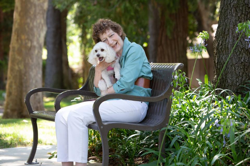 women sitting on an outside bench smiling and hugging her dog