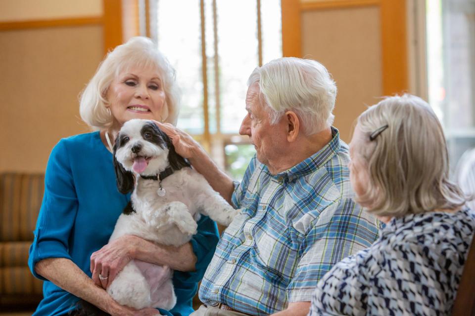 Three residents smiling and petting a dog