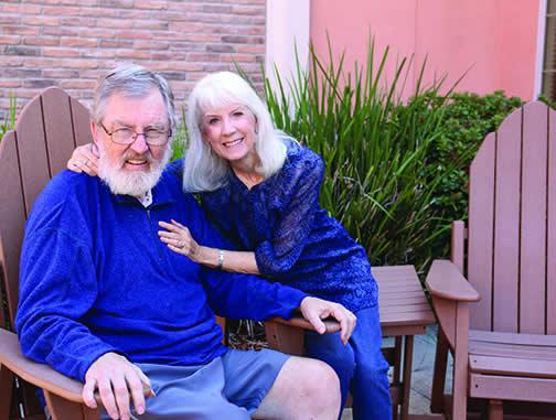 Smiling Eskaton resident Mark Silzer with his wife Barbara sitting outside